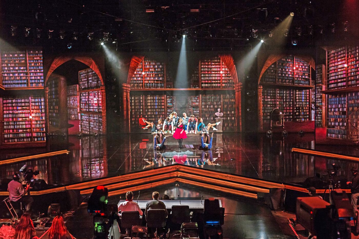 Arched bookshelf dvLED walls wrapping a stage in TRUE dvLED, dancers and camera crew at work
