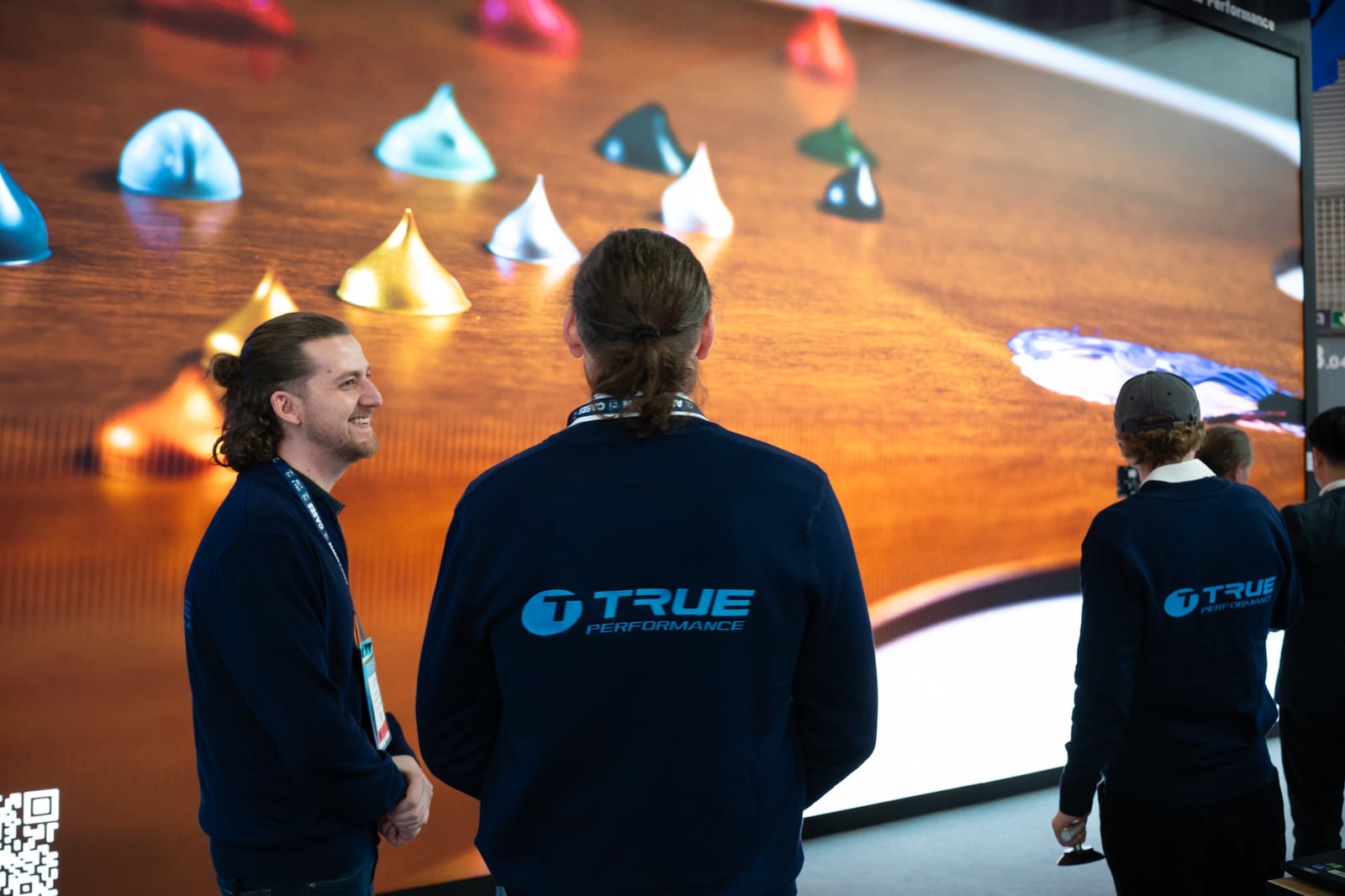 Two TRUE Performance engineers in front of a TRUE dvLED wall rendering colored paint drops on a wooden surface at a trade show