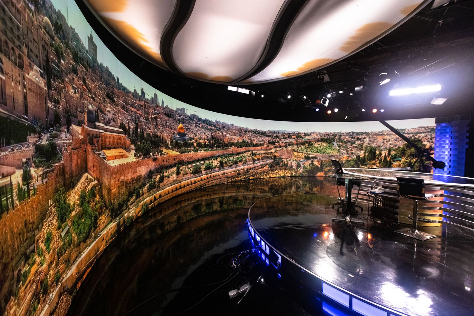 Curved TRUE dvLED studio dvLED wall showing a panoramic daylight cityscape behind a glass presenter desk