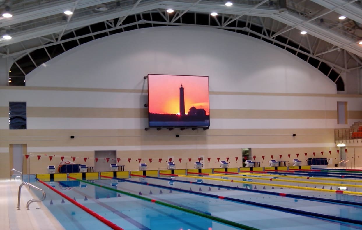 Indoor competition swimming pool with a TRUE dvLED screen on the dvLED wall showing a sunset scene